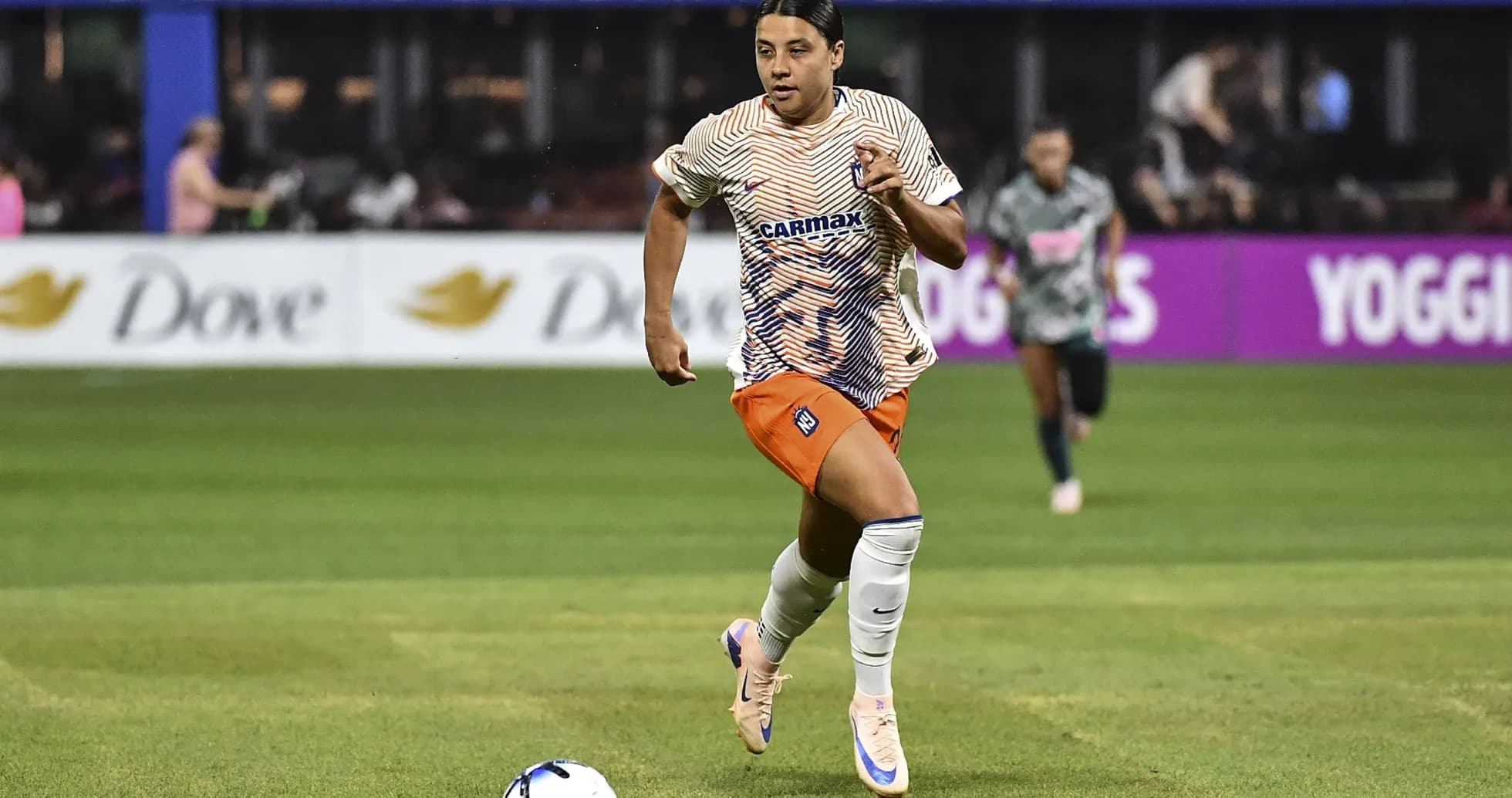 Jugadora corriendo con balón en el campo de fútbol