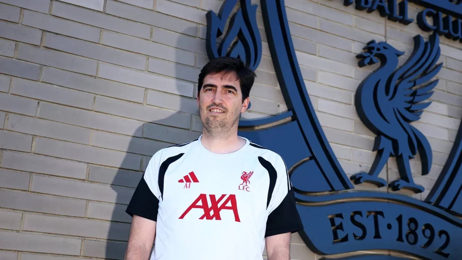 Entrenador posando frente al emblema del Liverpool