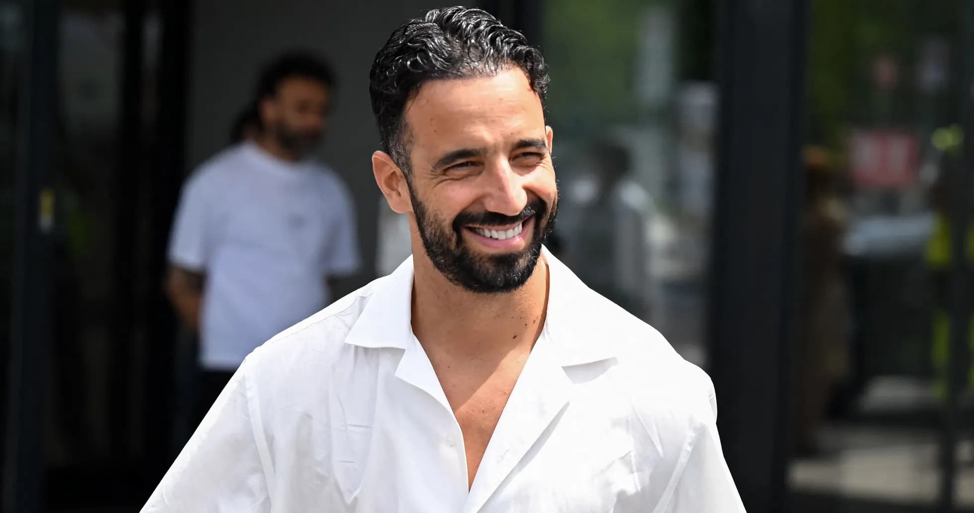 Hombre sonriente con camisa blanca saliendo de un edificio